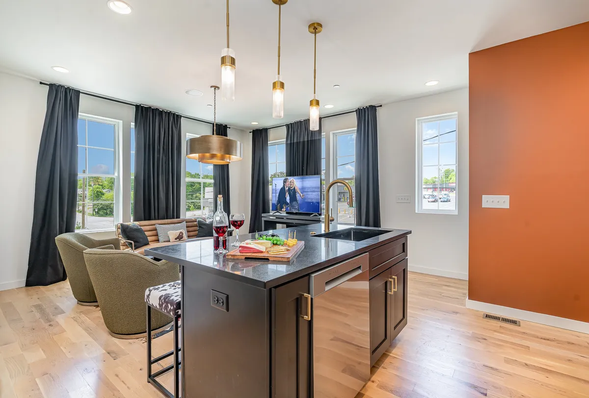 This interior shot focuses on a bright, inviting kitchen and dining area. The kitchen island and adjacent dining space are complemented by large windows that fill the room with natural light. A television is also visible, reinforcing the idea of integrated entertainment and meal prep spaces.