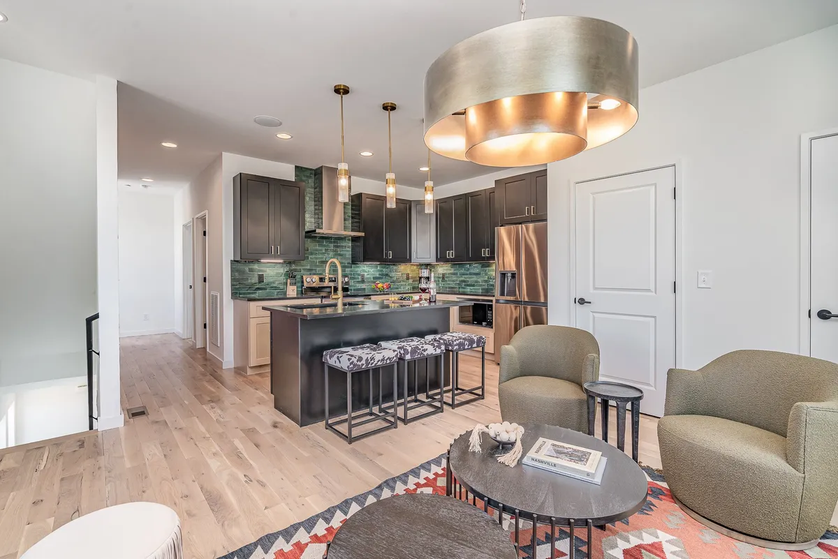 A stylish, contemporary kitchen with a central island, colorful backsplash, pendant lighting, and an adjacent comfortable seating area. The space is designed to encourage cooking, entertaining, and relaxed interaction among guests.