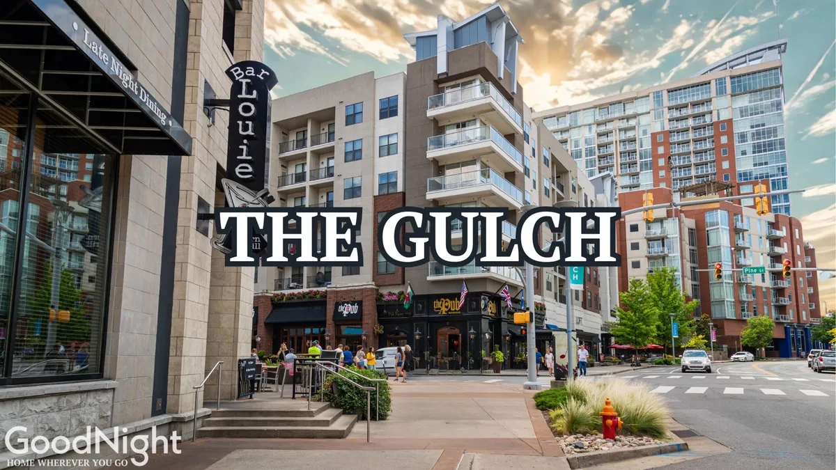 A lively street scene in The Gulch neighborhood, featuring Bar Louie, The Gulch sign, and modern apartment buildings. People are seen dining at outdoor tables and strolling the vibrant streets, with visible activity that hints at nightlife and urban energy.