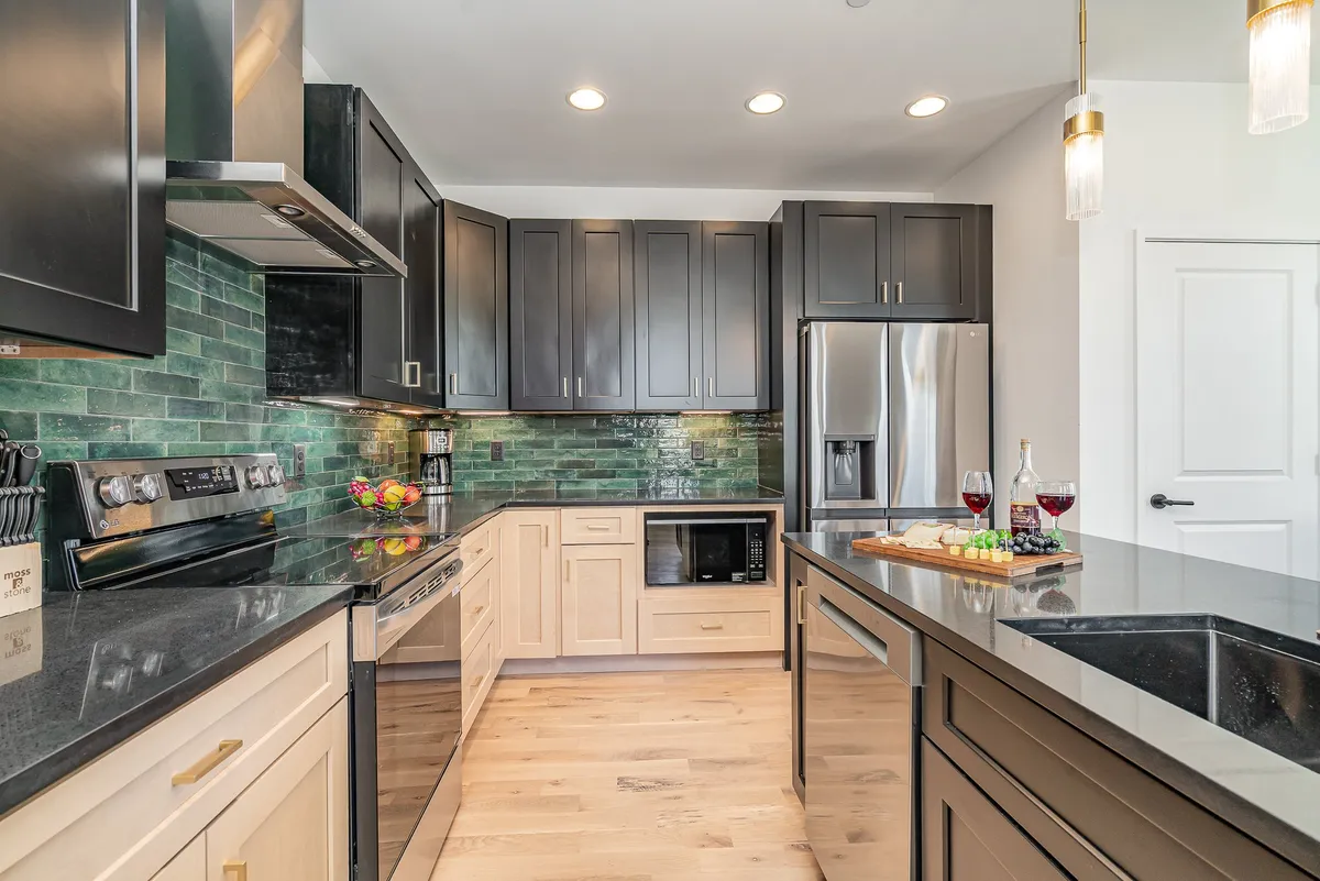 A sophisticated kitchen scene featuring black and green cabinetry, stainless steel appliances, elegant countertops, and a set table with wine glasses and a cheese platter. The space is both functional and stylish, reflecting thoughtful attention to detail.