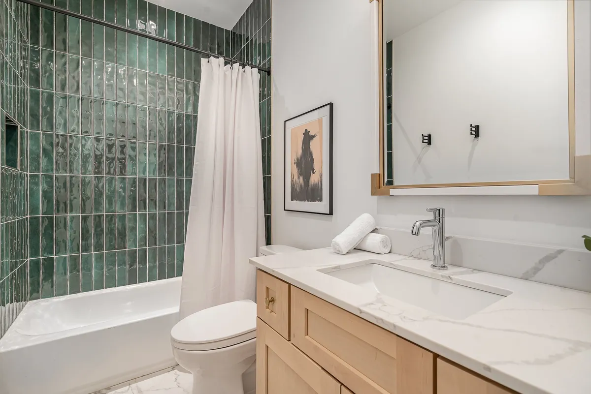 The bathroom showcases green tile walls, a white bathtub, a modern sink, and framed artwork, creating a tranquil environment for relaxation and daily routines.
