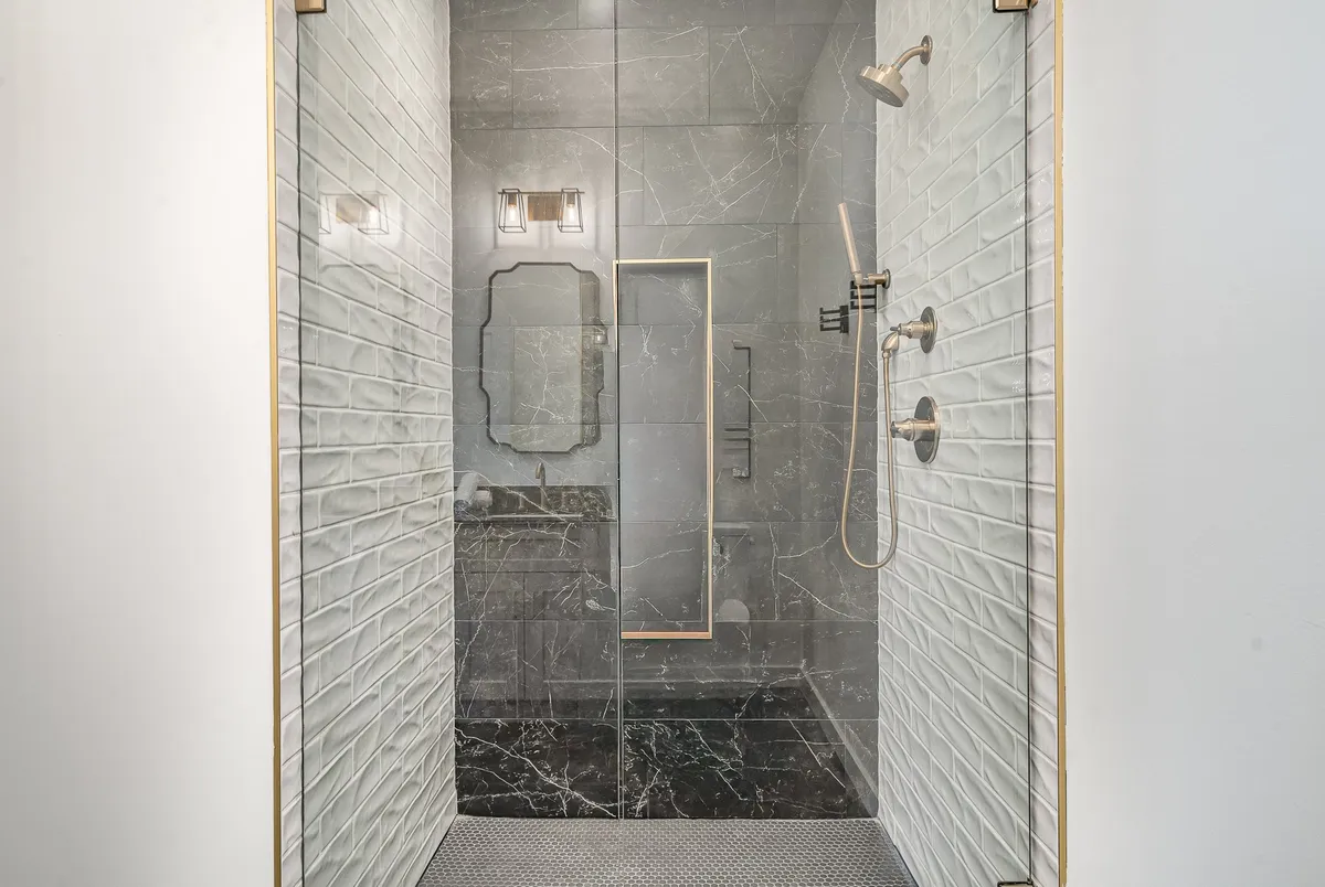 The bathroom boasts a pristine glass shower enclosure, sleek marble tiles, modern fixtures, and a decorative mirror. The setting is serene and evokes a spa-like ambiance, ideal for rejuvenation and self-care.